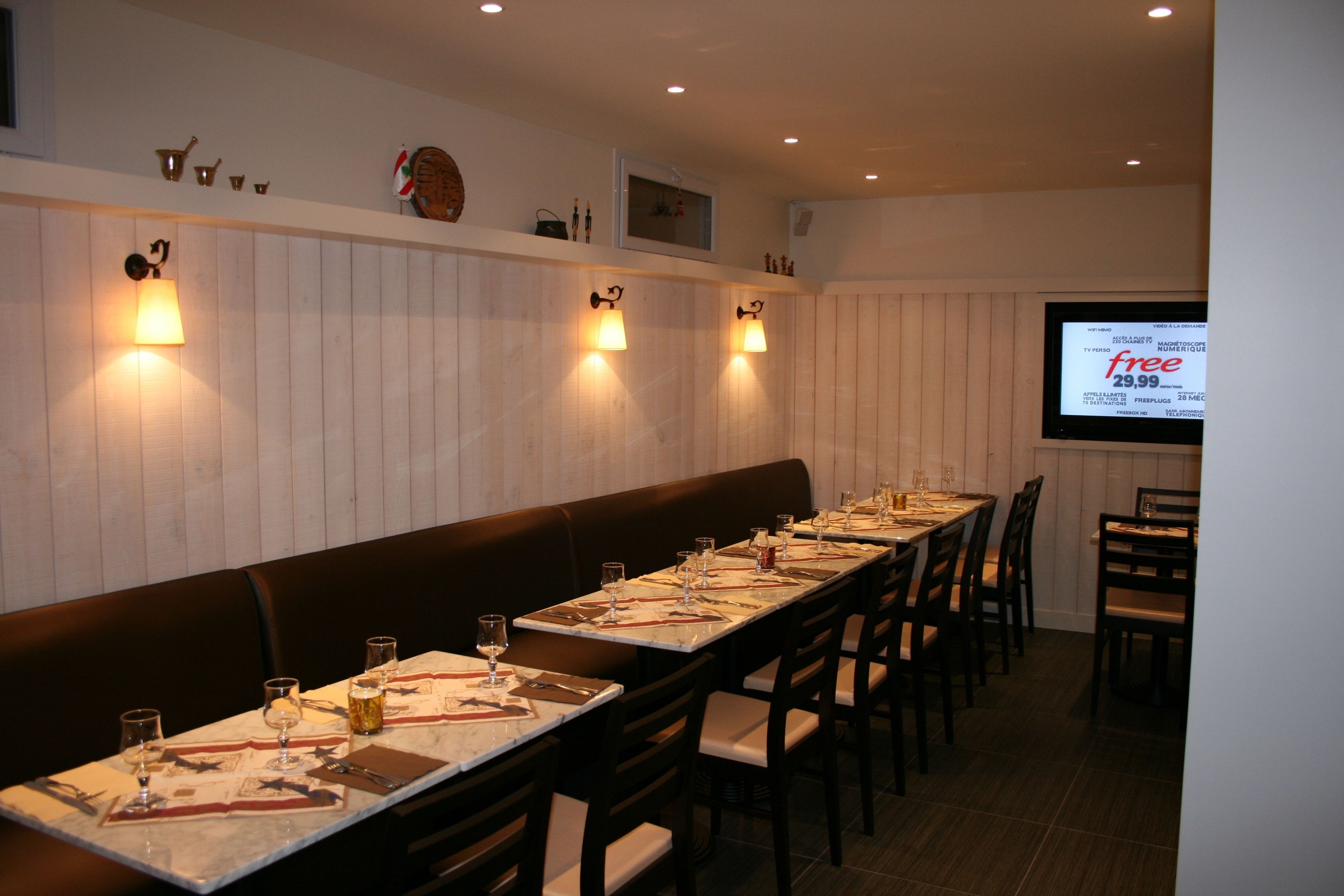 Um restaurante com mesas compridas dispostas para refeições, iluminação fixada na parede e uma tela de projeção exibindo um menu.