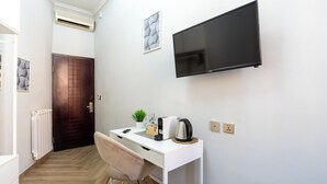 A modern room with a white desk, a mounted TV, a radiator, a door, and a small plant. - Giusi Rooms - Aetheria Esquilinus Guesthouse (Rome)