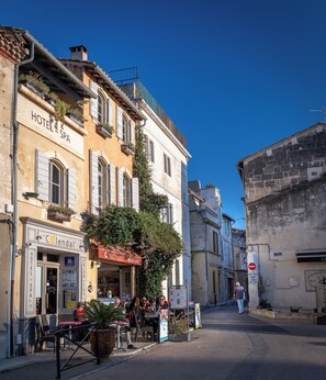 A street with a hotel and cafe, outdoor seating, and a pedestrian. - Hotel Spa Le Calendal (Arles)