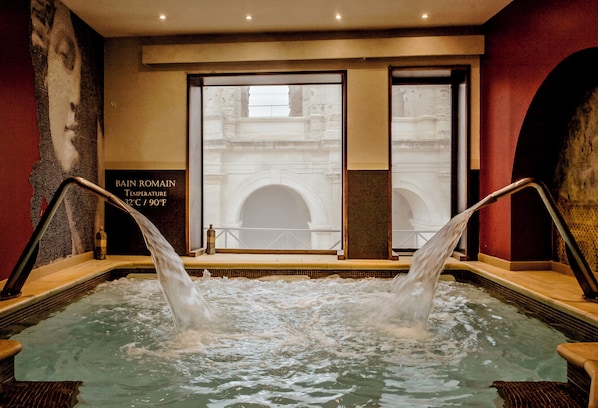 A hot tub with water jets, a temperature sign, and a view of a building through a window. - Hotel Spa Le Calendal (Arles)