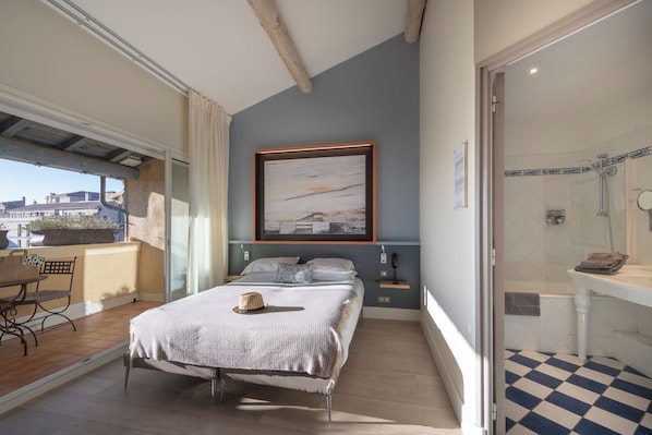 A bedroom with a bed, a nightstand, a framed picture on the wall, and a view of the city through a sliding door. - Hotel Spa Le Calendal (Arles)