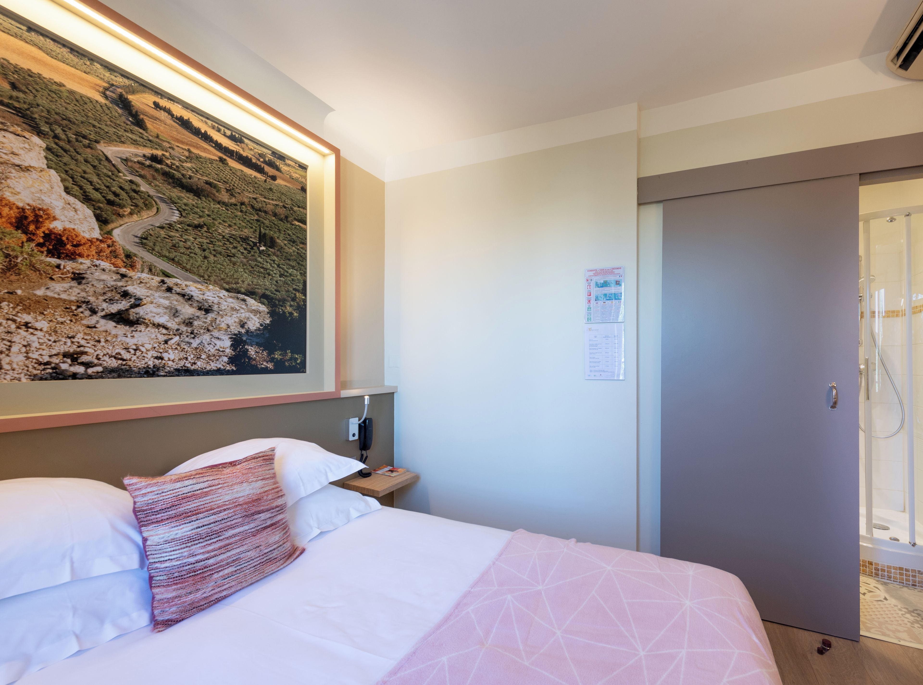 Una habitación de hotel con una cama, una mesita de noche, un teléfono, una puerta y un cartel en la pared.