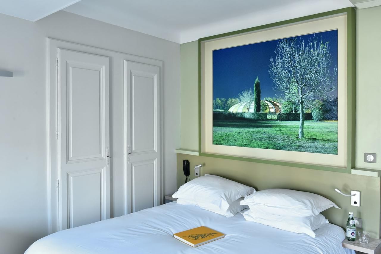 A hotel room with a bed, a window with a view of a garden, and a telephone on the nightstand.