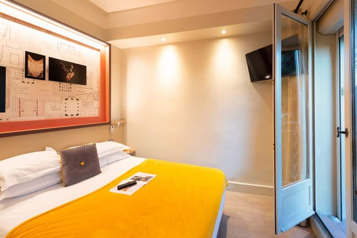 Habitación de hotel con cama, televisor montado en la pared y puerta que da a un balcón.