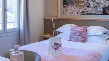 Une chambre d’hôtel avec un lit, un tableau au mur, une table de chevet avec un vase en verre et un sac posé sur le lit.