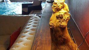 Une table en bois avec une lampe et un objet décoratif, un banc blanc avec coussin, et une vue sur l’espace piscine.