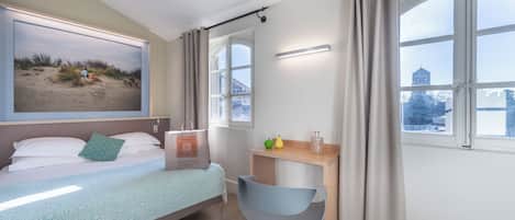 Una habitación de hotel con cama, escritorio, silla, ventana con cortinas y un cuadro en la pared.