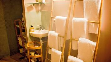 A bathroom with a glass shelf holding toiletries, a white sink, and a wooden ladder with towels.