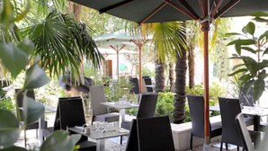Un espace de restauration en plein air, avec des tables et des chaises, entouré de palmiers et de verdure.