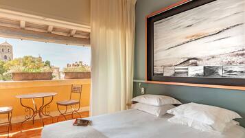 Habitación de hotel con cama, un cuadro grande, vista a un paisaje urbano y balcón con mesa y sillas.