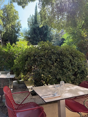 An outdoor dining area with tables and chairs, surrounded by dense greenery and trees. - Hotel Spa Le Calendal (Arles)