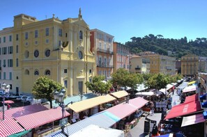 A bustling street market with colorful tents and a prominent yellow building with classical architecture. - Logis Hôtel Villa Victorine (Nice)