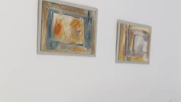 A bed with white bedding, two abstract paintings on the wall, and a small plant on the nightstand.