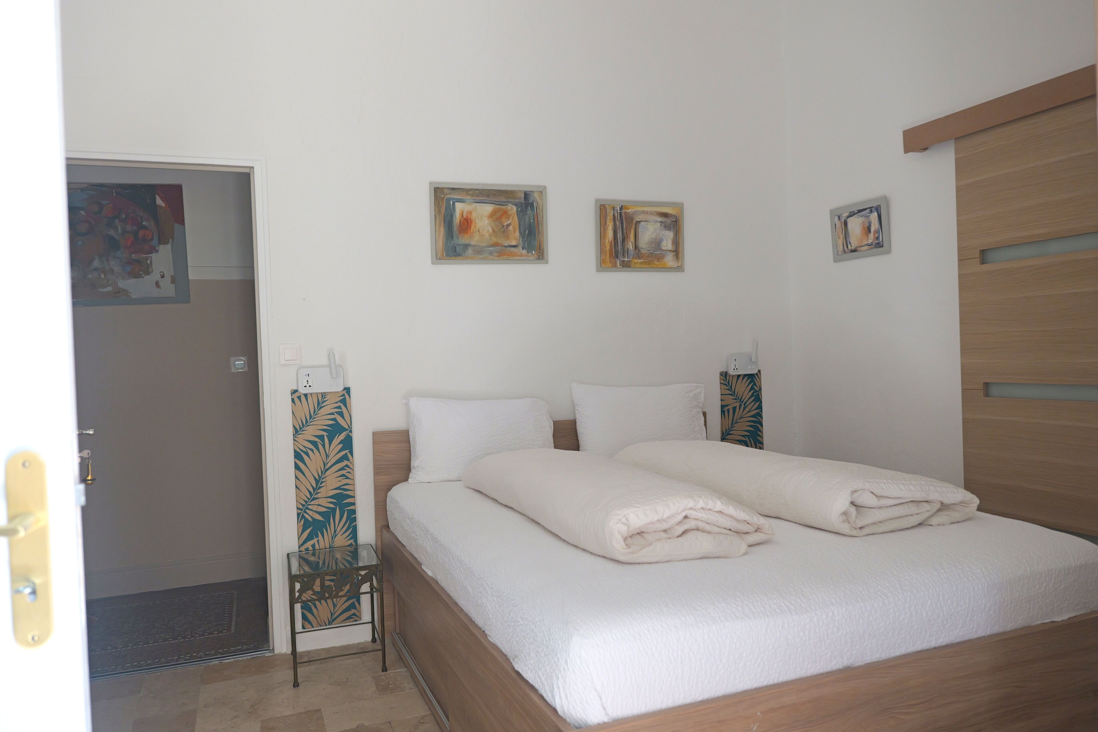 Un dormitorio con cama, puerta y dos cuadros colgados en la pared.