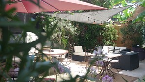 An outdoor patio with a round table, chairs, and a large umbrella providing shade. - Logis Hôtel Villa Victorine (Nice)