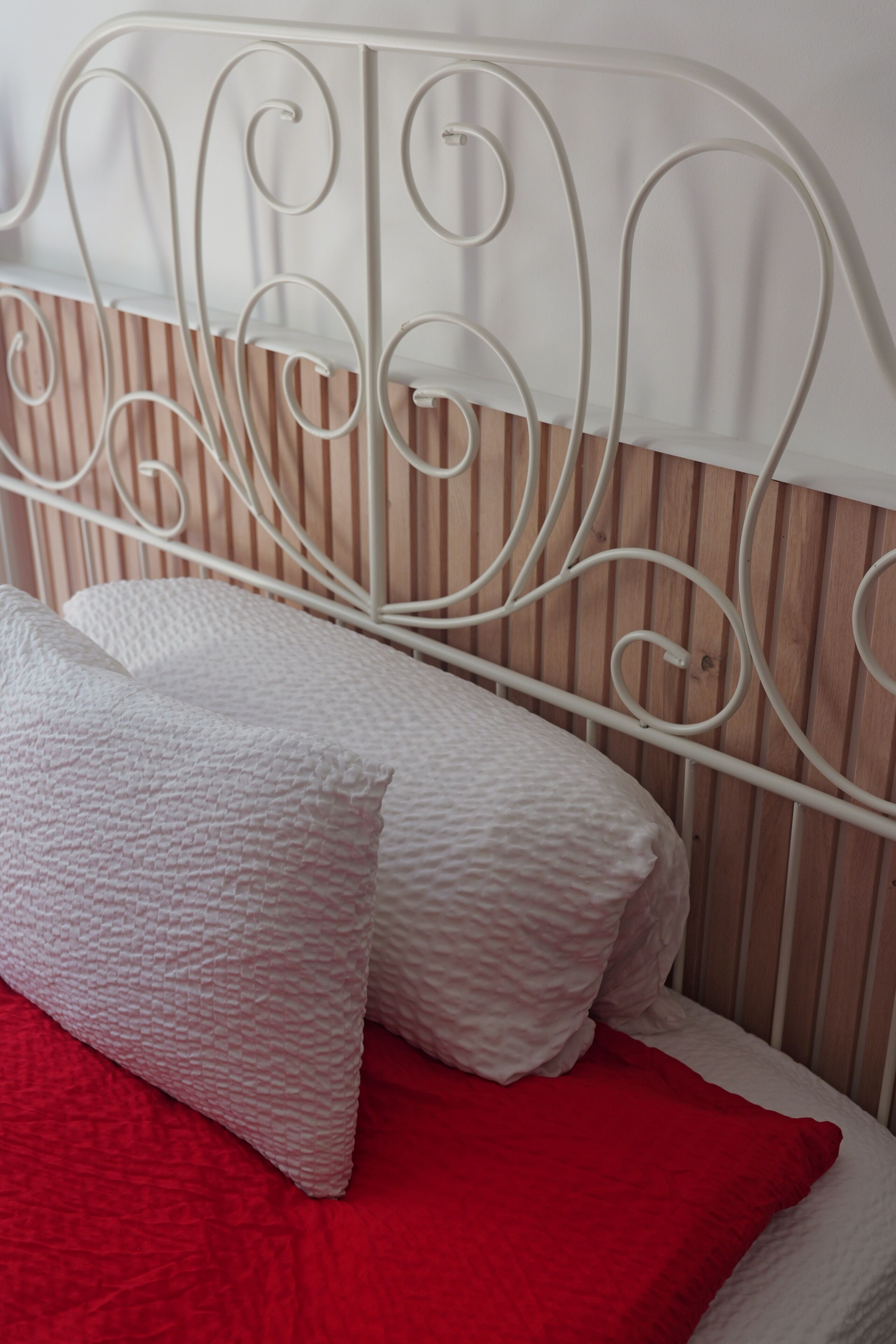 Una cama con cabecera de metal blanco, dos almohadas y una colcha roja.