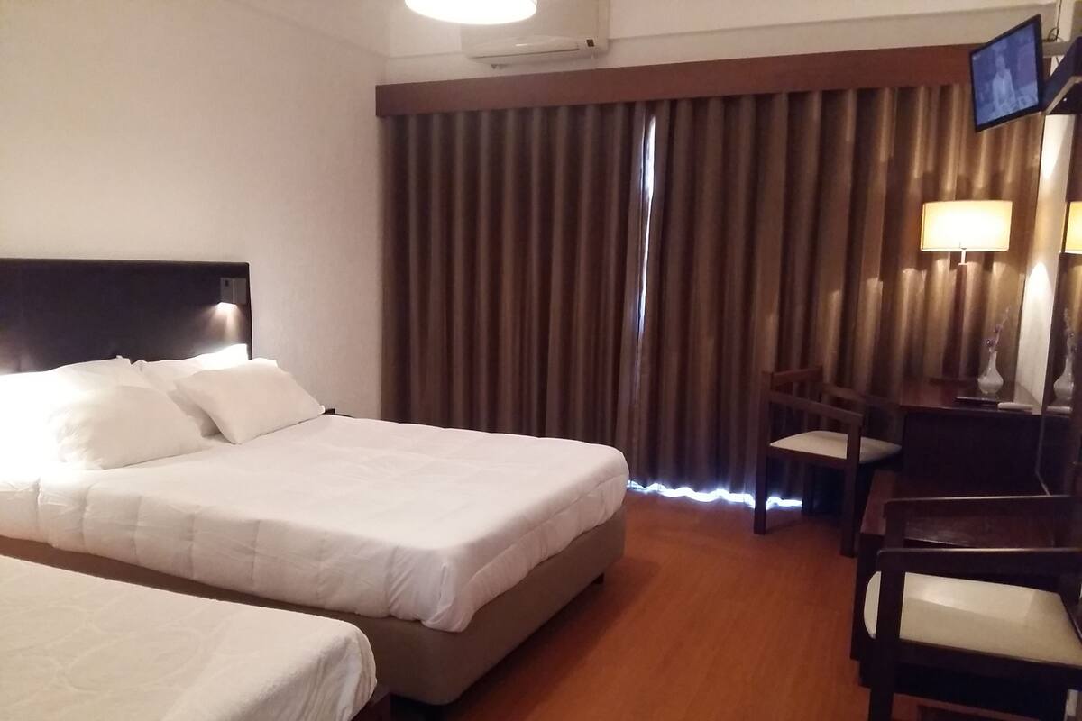 A hotel room with a large bed, a smaller bed, a desk with a chair, and a TV mounted on the wall.