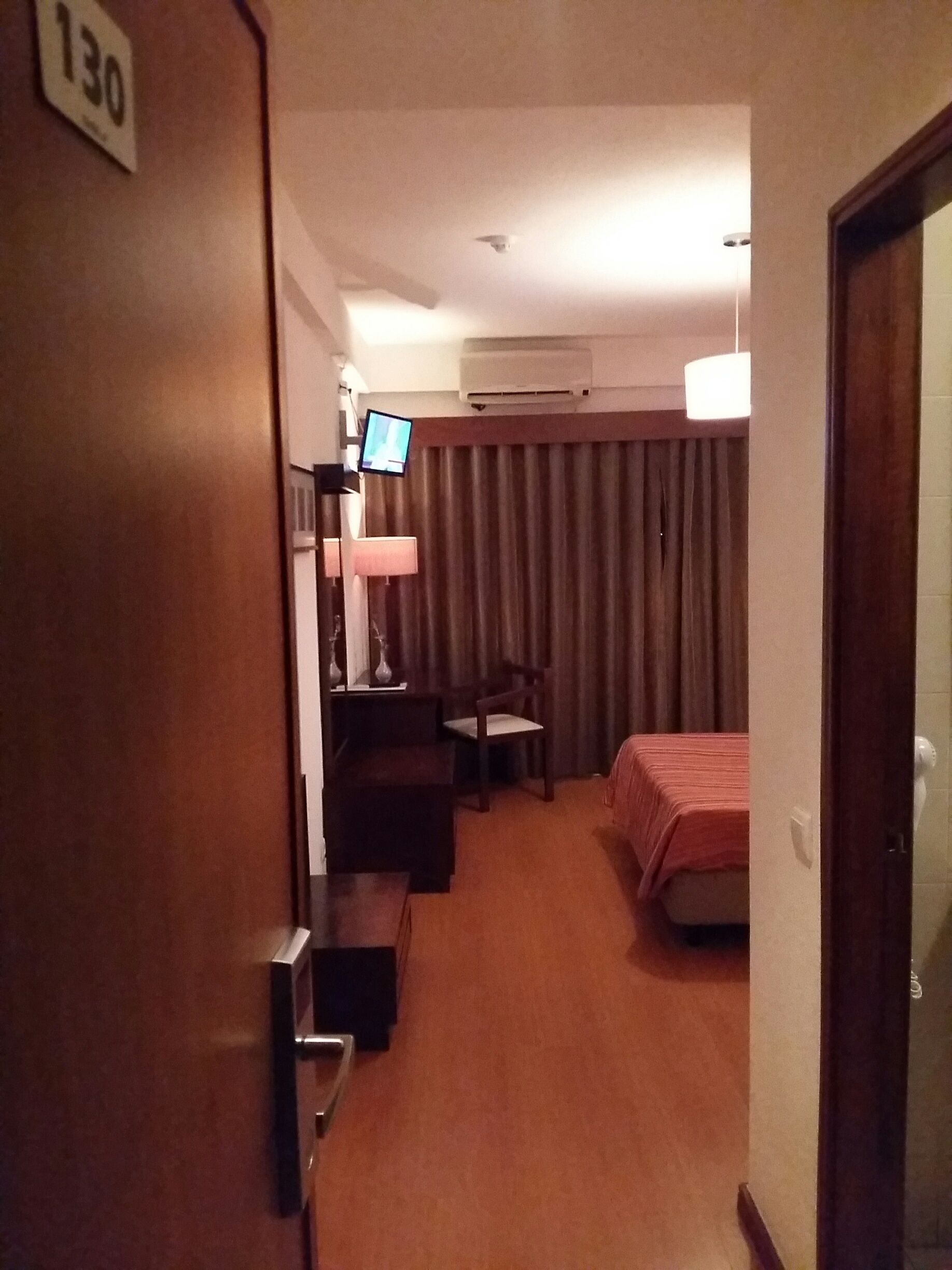 A hotel room with a bed, a desk, a chair, a television, and a window with curtains.