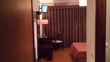 A hotel room with a bed, a desk, a chair, a television, and a window with curtains.