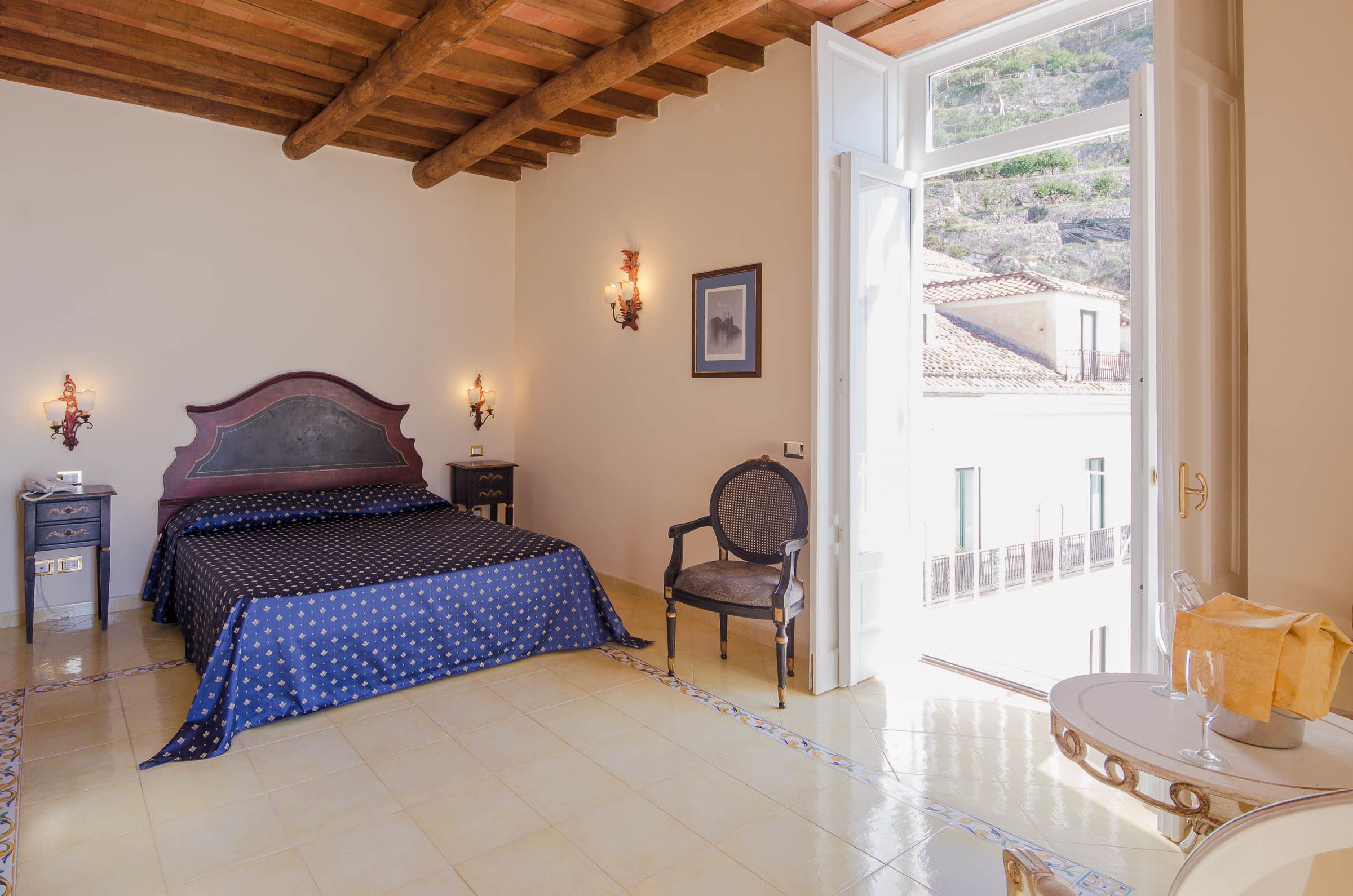 A bedroom with a large bed, a chair, a bedside table, and a view of the outside.