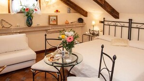 Une chambre confortable avec un grand lit, un canapé, une petite table ronde ornée d’un vase de fleurs et un plafond en bois.