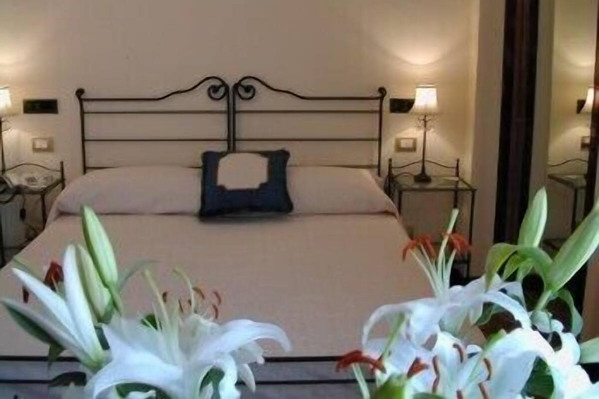 A hotel room with a bed, two bedside tables, and a nightstand. There are two lamps on the bedside tables.