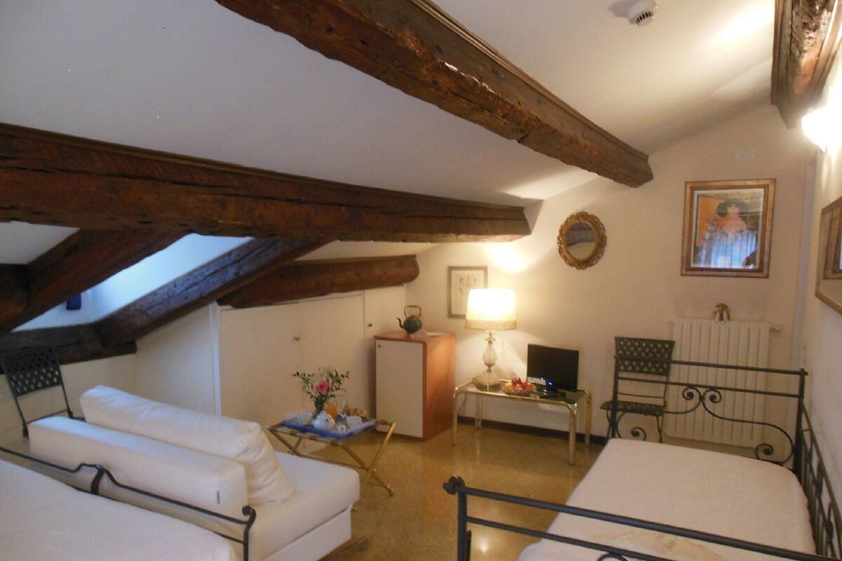 A room with a loft bed, a sofa, a small table with a lamp, and a radiator.