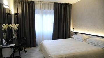 Ein Hotelzimmer mit Bett, Schreibtisch und Stuhl. Ein Fenster mit Vorhängen und ein Blumenstrauß auf dem Schreibtisch.