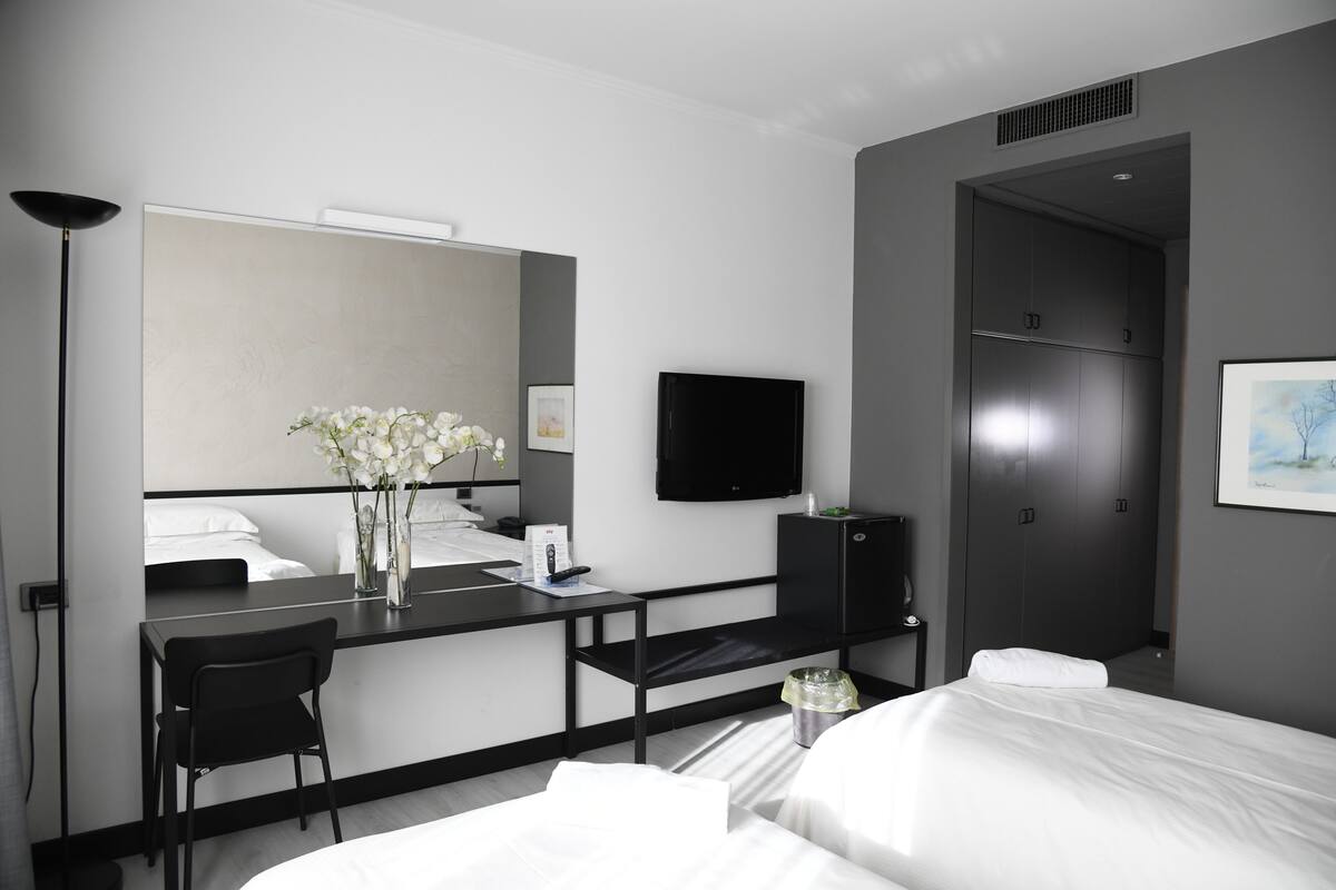 A modern hotel room with a bed, a desk with a chair, a flat-screen TV, a mirror, and a wardrobe.