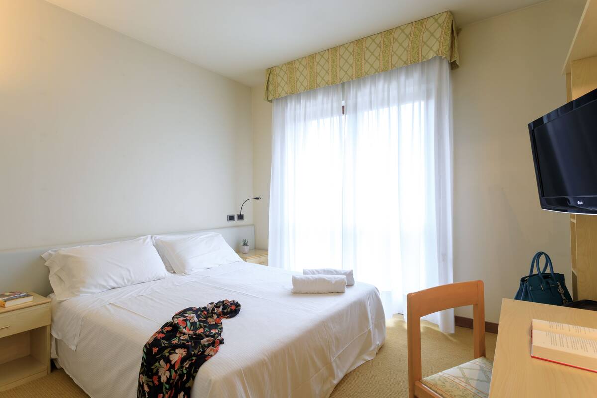 A hotel room with a bed, a chair, a desk, a television, and a window with curtains.