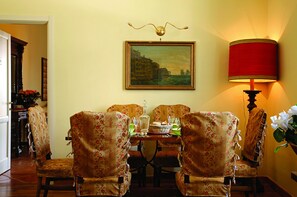 A dining area with floral upholstered chairs, a table set with glassware, a painting on the wall, and a red lamp. - Luna Caprese (Naples)