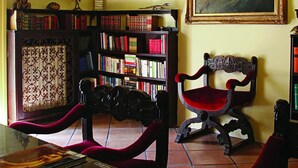 A room with a bookshelf, a chair, and a table with books and a framed painting. - Luna Caprese (Naples)