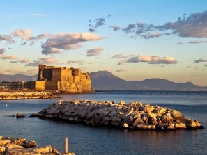 A coastal fortification with a large stone wall and a smaller building, surrounded by rocky terrain and a calm sea. - Luna Caprese (Naples)