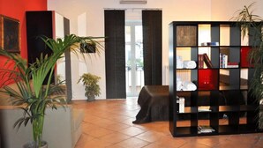 A modern living room with a black sectional sofa, a large potted plant, a black bookshelf, and a red accent wall. - Luna Caprese (Naples)