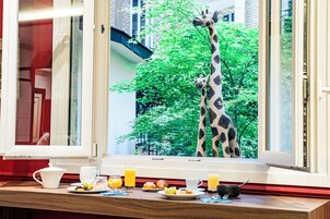A breakfast table with plates, cups, and juice glasses, and a view of two giraffes outside a window.