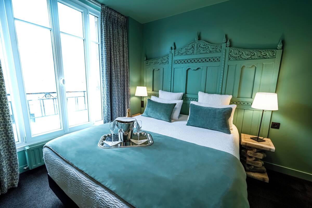 A neatly made bed with a tray of glasses and a pitcher, a headboard with intricate carvings, and two bedside lamps.