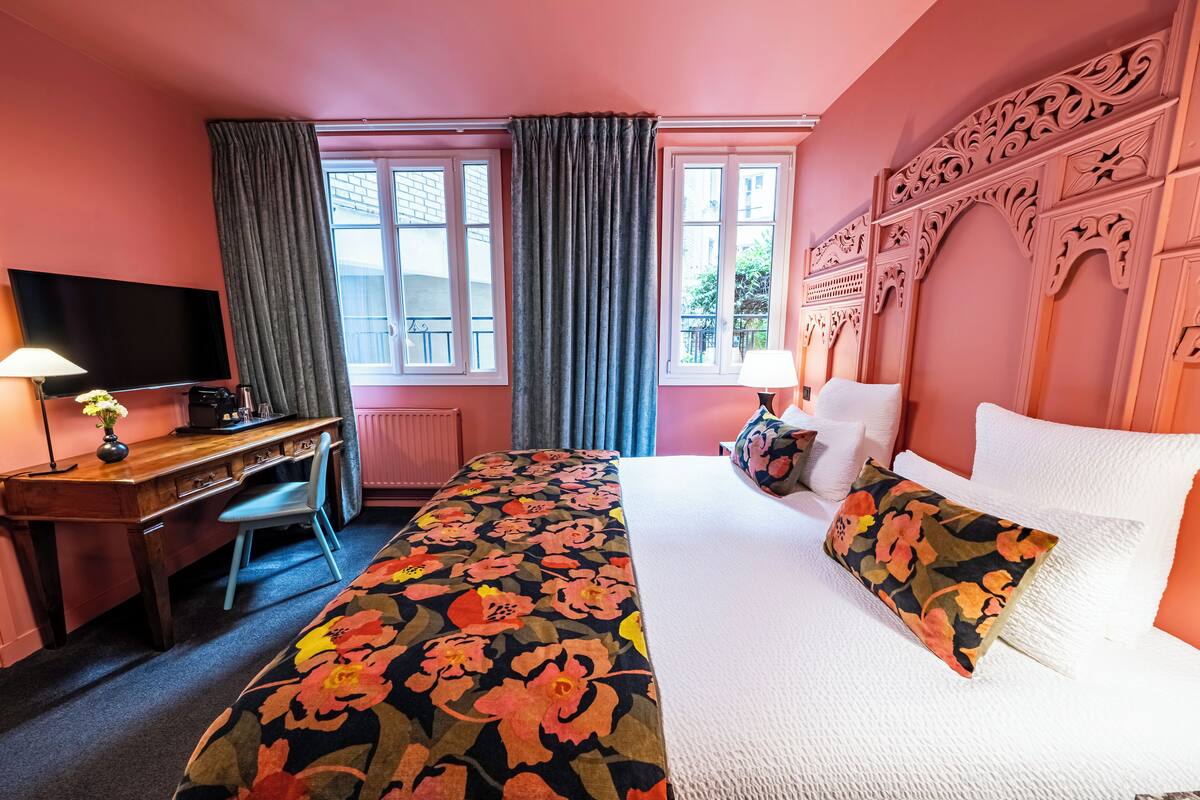 A hotel room with a bed, a desk, a television, and a window with curtains.