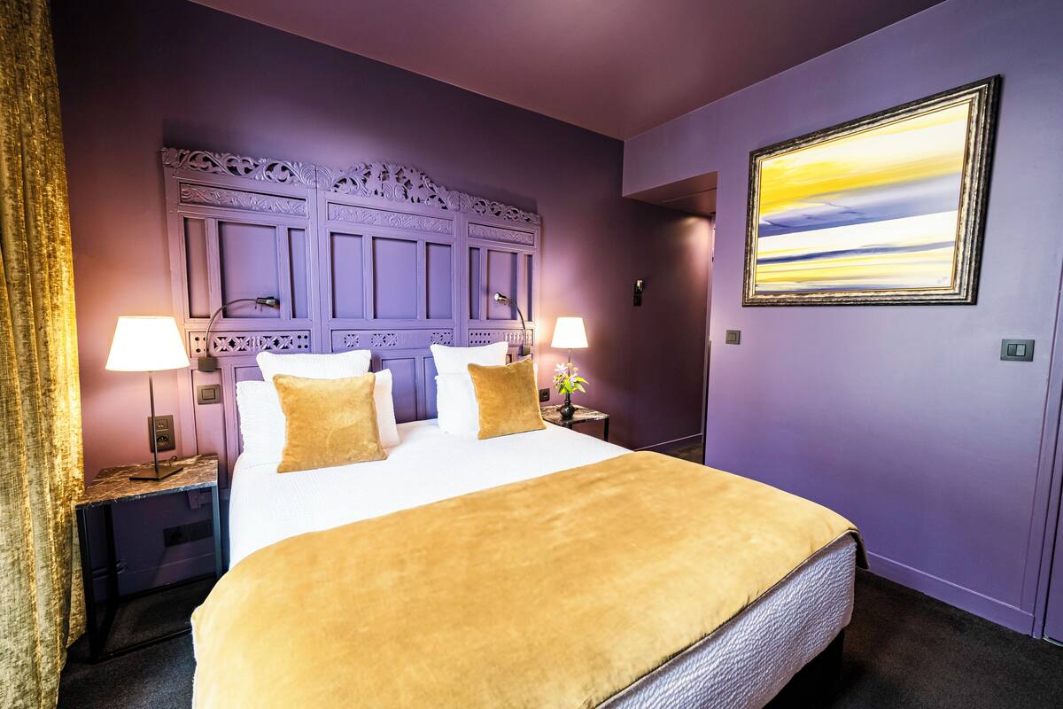A hotel room with a large bed, two bedside tables with lamps, a decorative headboard, and a framed picture on the wall.
