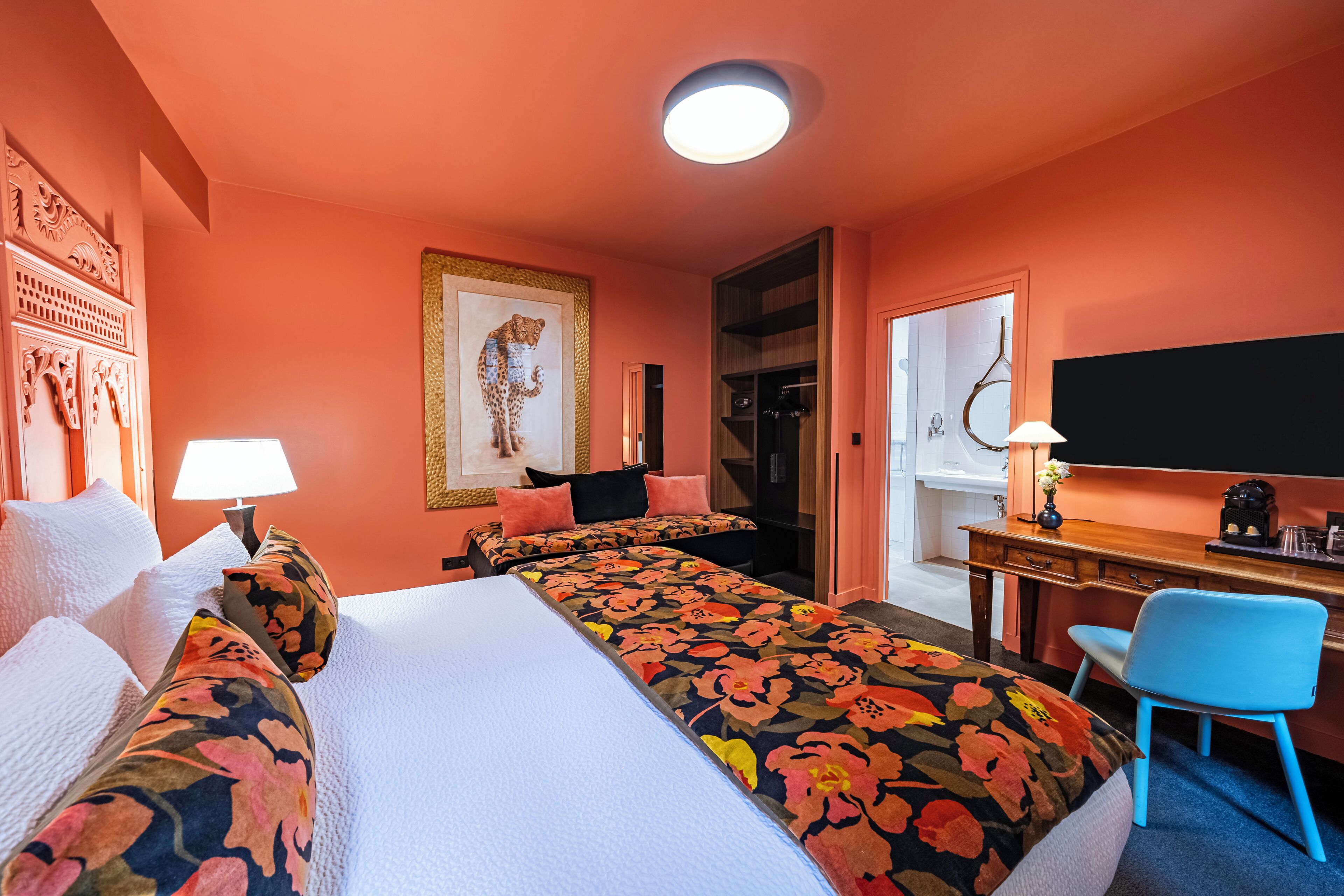 Habitación de hotel con una cama grande, un escritorio con silla, un espejo y una puerta que da a un baño.