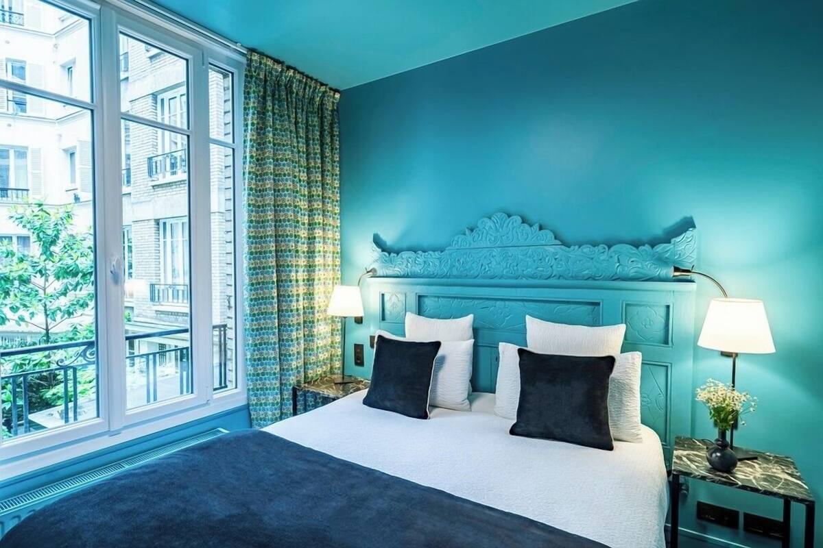 A bedroom with a large bed, a teal-colored headboard, and a view of a balcony.