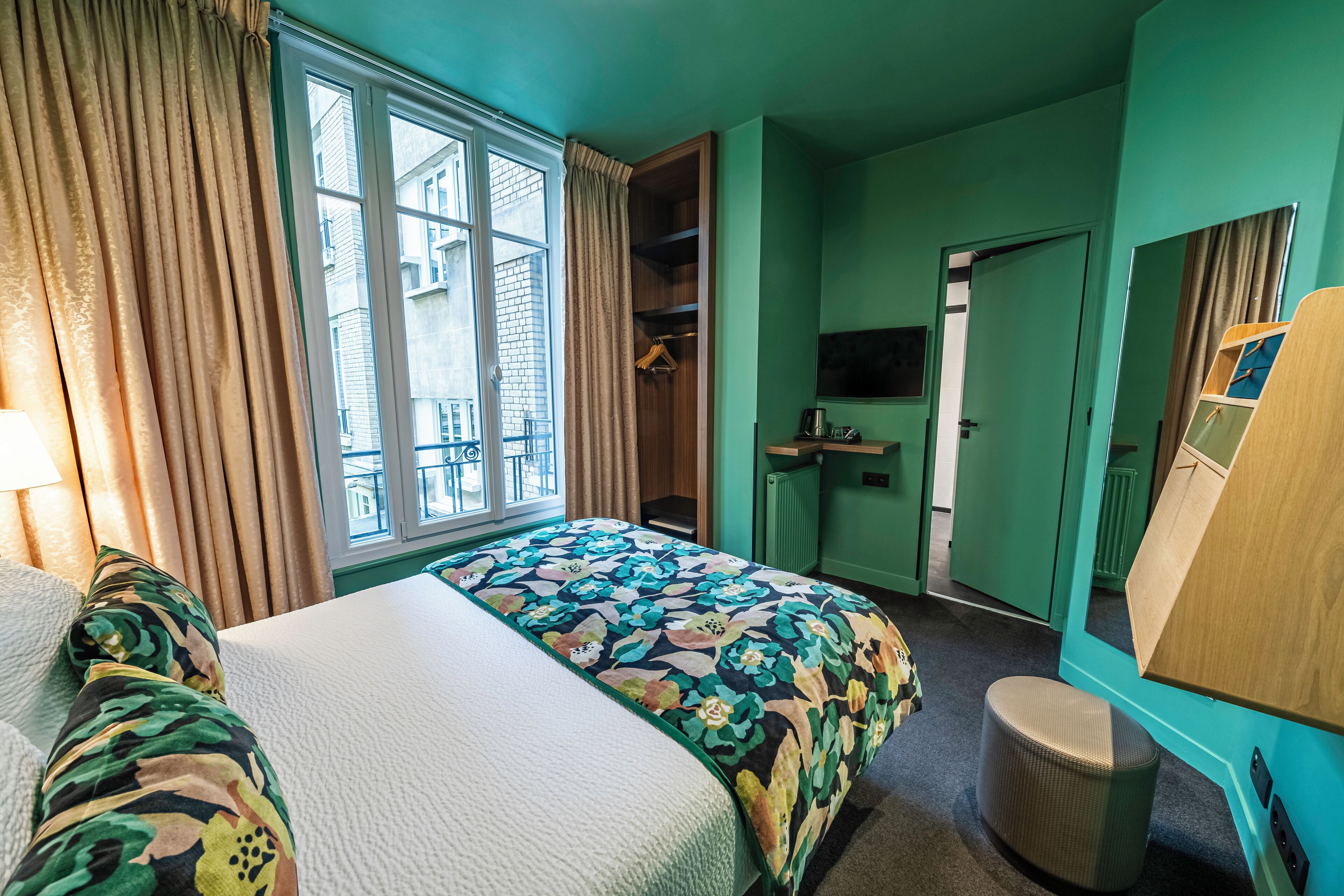 A hotel room with a bed, a wardrobe, a mirror, and a window with curtains.