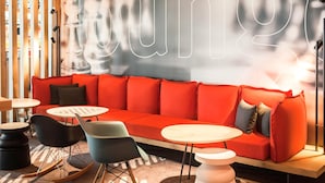 Un espacio de descanso moderno con un sofá rojo, sillas negras y azules, y una mesa redonda.