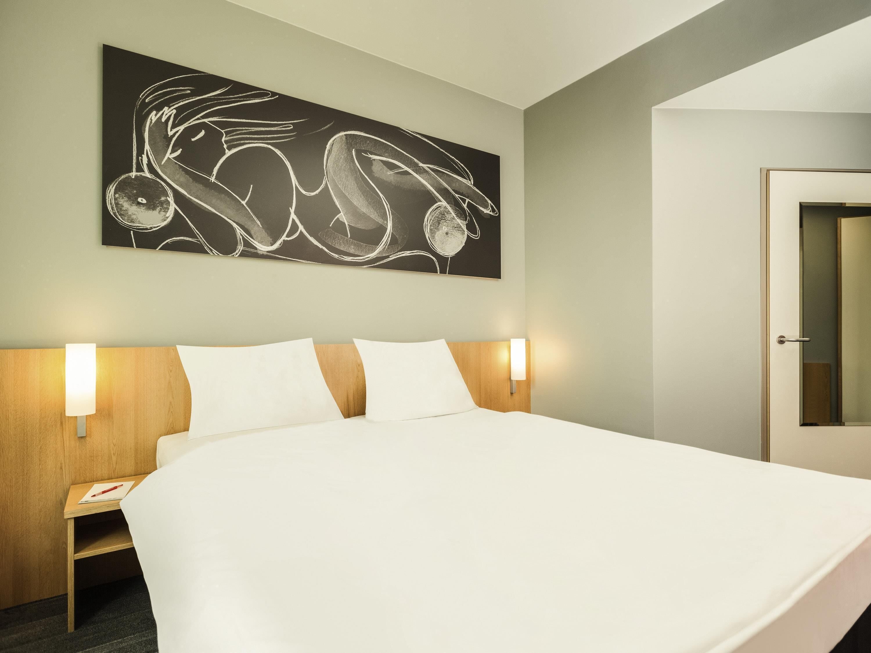 Ein Hotelzimmer mit einem großen Bett, zwei Nachttischen, einem Wandbild und einer Tür.