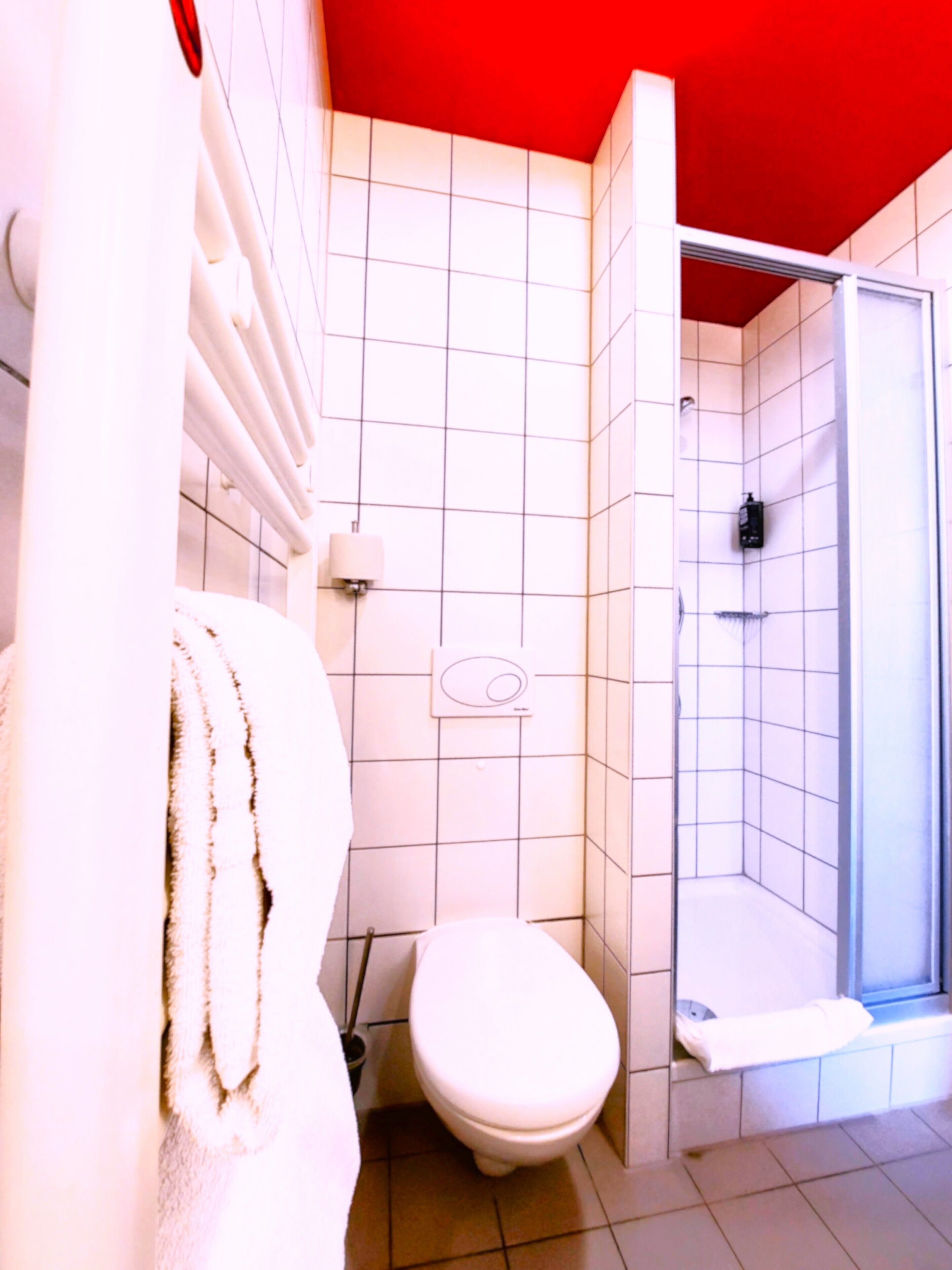 Une salle de bain avec des toilettes blanches, une douche dotée d’une porte en verre et un porte-serviettes.