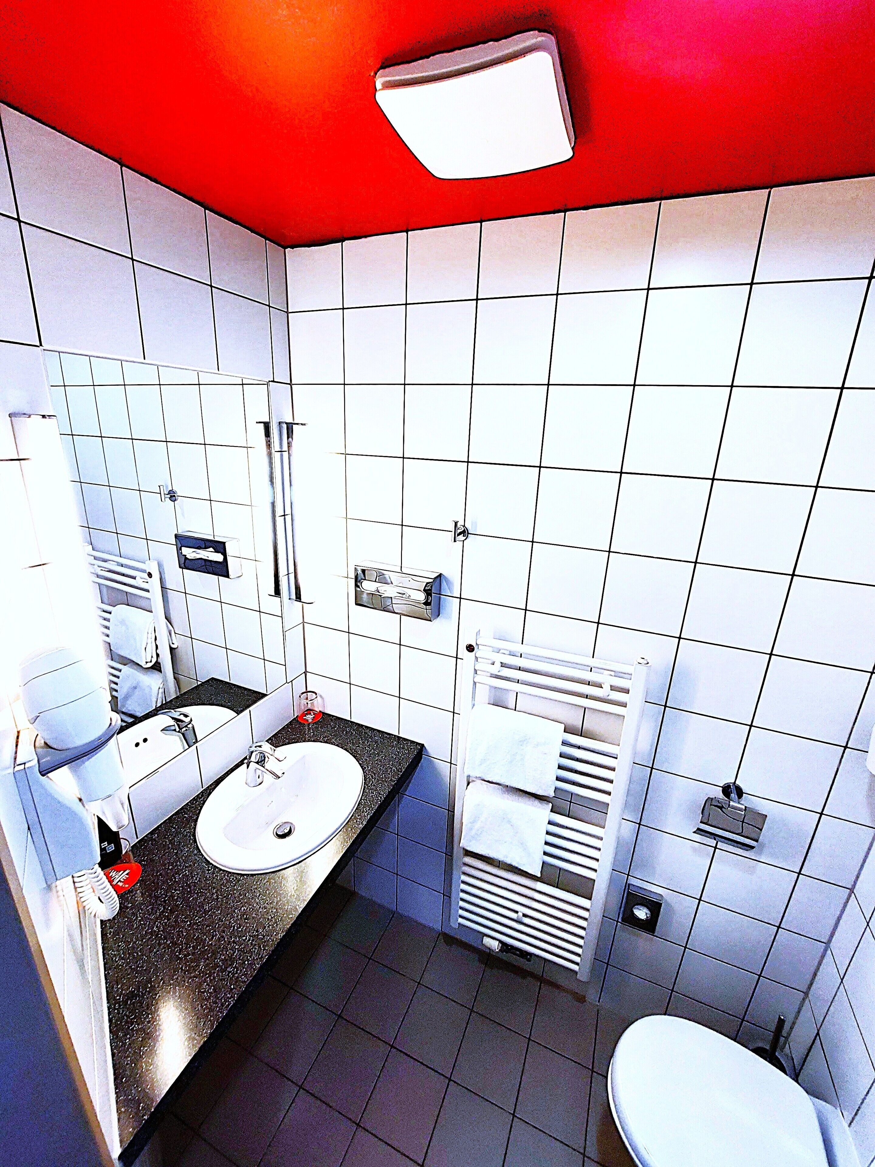 A modern bathroom with a black countertop, white sink, and a red ceiling.