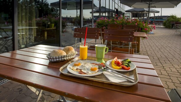 Un espacio de comedor al aire libre con mesas y sillas de madera, una bandeja con artículos para el desayuno y sombrillas.
