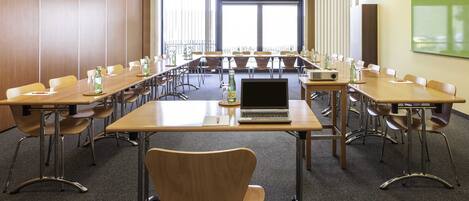 A conference room with long tables, chairs, a laptop, and a projector.