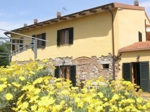 A yellow building with stone accents and green shutters, surrounded by yellow flowers. - Il Gelso (Santa Luce)