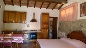 Quarto compacto com cama, uma mesinha e uma área de kitchenette.