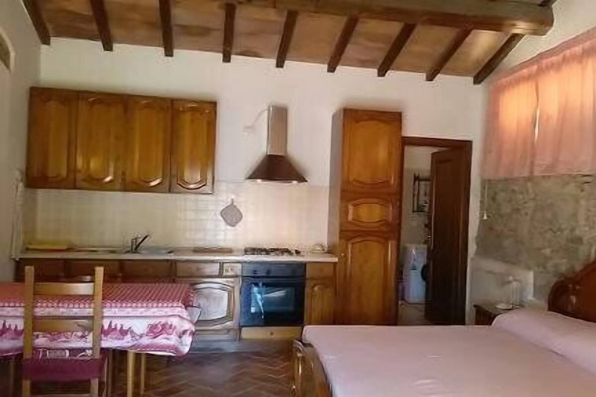 Een kleine slaapkamer met een bed, een tafeltje en een kitchenette.